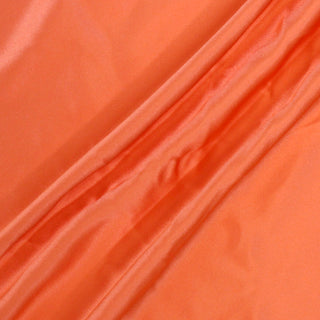 three draped lines of coral colored silk charmeuse fabric, demonstrating the high shine and lightweight, fluid drape