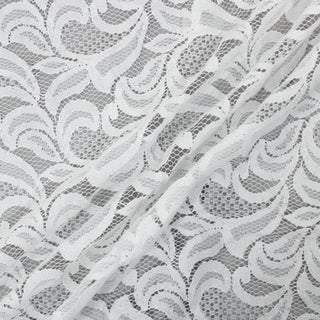 three diagonal lines arranged of white scroll-patterned lace, photographed on top of a light grey fabric
