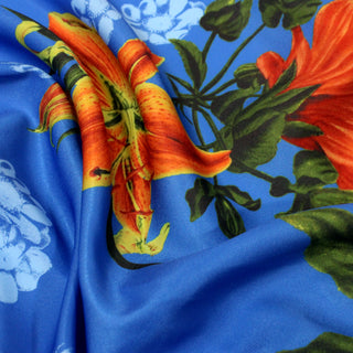 close up of tropical flower printed synthetic fabric with orange flowers on a blue ground. Plainweave with a subtle sheen, and the fabric is rumpled to show the lightweight and drapey hand
