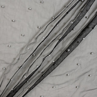 diagonal lines draped of a black mesh fabric across a white surface. the fabric has white faux pearls beaded sparsely across its surface