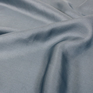 close-up of a dusty blue silk mikado fabric, detailing its drape and twill weave