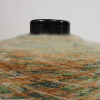 close-up of a multi-color cone of fine-gauge, mohair yarn, in shades of green and orange