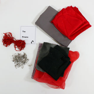 the contents of one holiday giftwrap kit: 2 folded yards of 2 different colored fabrics, 1/4 lb of festive colored fabric scraps, 8yds of ribbon, 1oz of safety pins, and a to-from tag