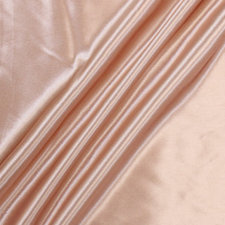 light pink colored charmeuse fabric arranged with three diagonal peaks across it to demonstrate its high-shine face and drapey hand