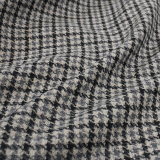 close-up of a soft wool houndstooth fabric, detailing the weave and showing its colors: a light stone grey, light blue, and dark grey