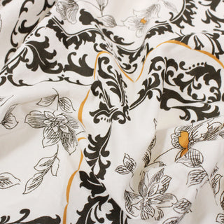 Close-up of fabric with dark brown and ochre colored floral and baroque blockprint patterns on an off-white ground