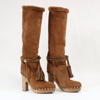 Pair of brown suede knee-high boots with tassels and platform sole on a white background