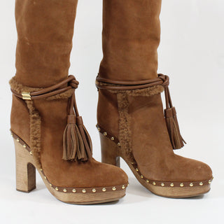Brown suede boots with tassels and stud details on a white background