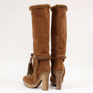 Brown suede knee-high boots with fur trim and decorative elements on a white background