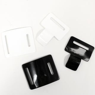 two large buckles made of plastic, one white and one black, with the two pieces of each separated to show how they close
