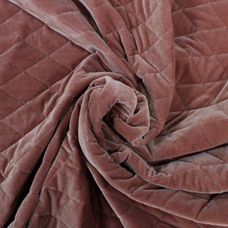 swirl of a dusty rose velour quilted batting fabric, demonstrating the heaviness of the drape